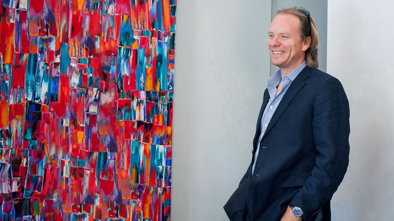 Darren Slavens standing beside a colourful abstract painting in the Slavens office