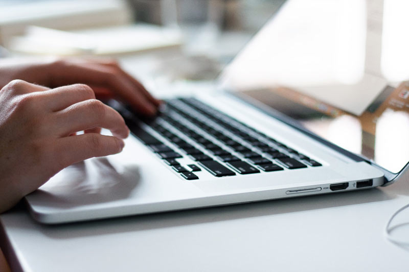 A person typing on a laptop at a bright desk